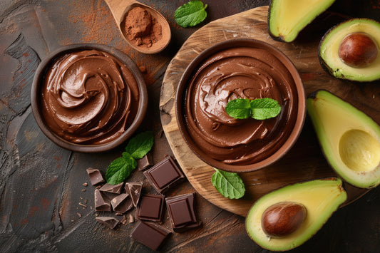 Two cups of chocolate mousse sitting beside halved avocados, garnished with mint